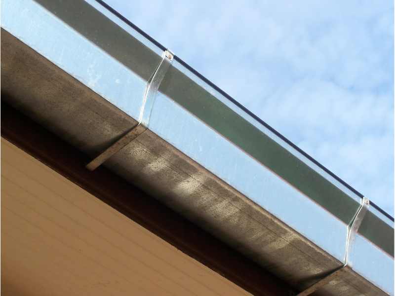 Technician standing on a ladder working on a gutter system along the roofline of a home surrounded by trees and landscaping
