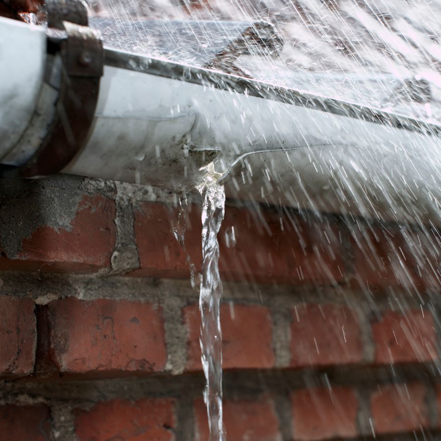 Close-up of a gutter leaking and overflowing with water spilling over the edge onto a brick wall