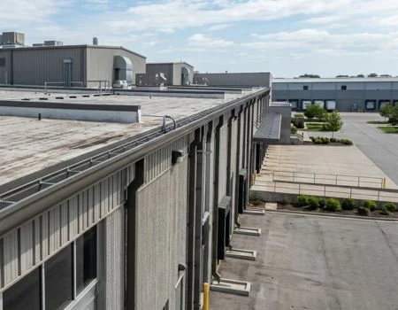 Large commercial or industrial building with a flat roof and long gutter system running along the edge, directing water through multiple downspouts