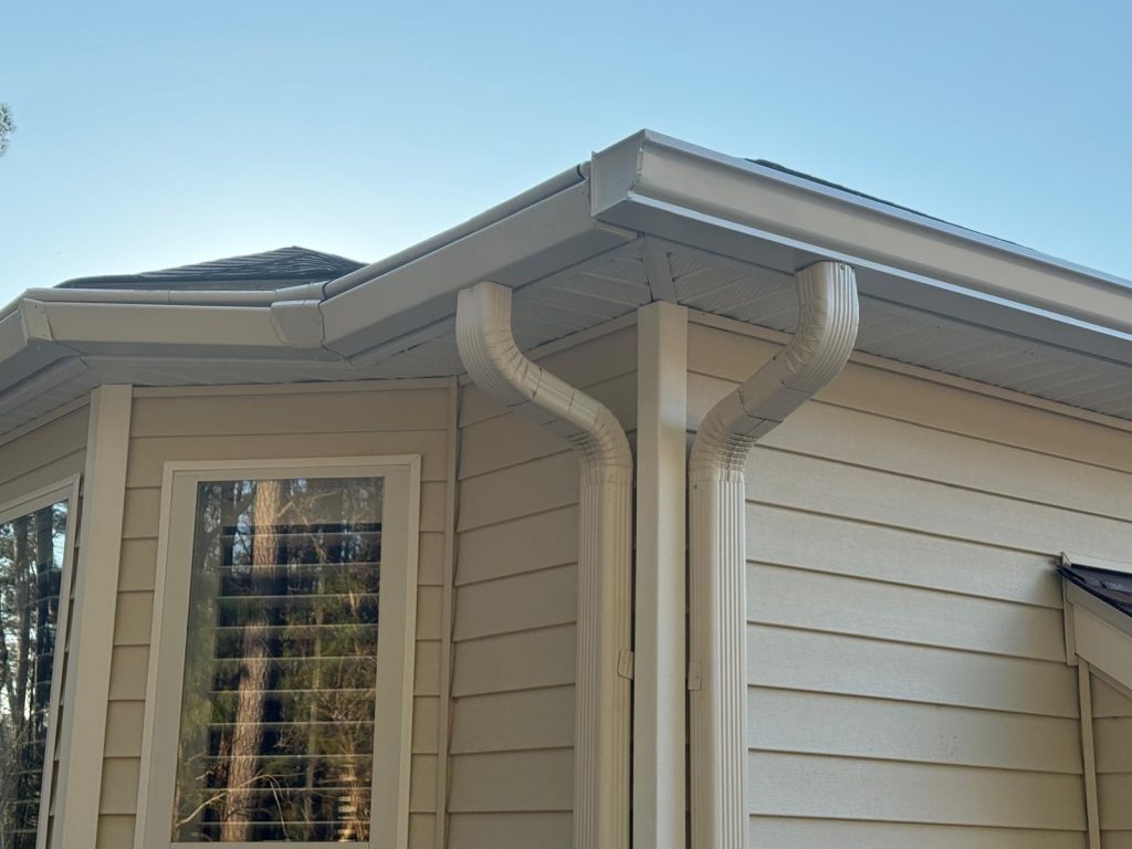 Close-up of a gutter system at a roof corner with two white downspouts directing water from the roofline