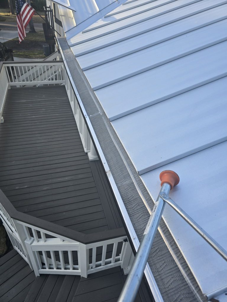 Close-up of a gutter guard system installed on a metal roof above a wooden deck and railing