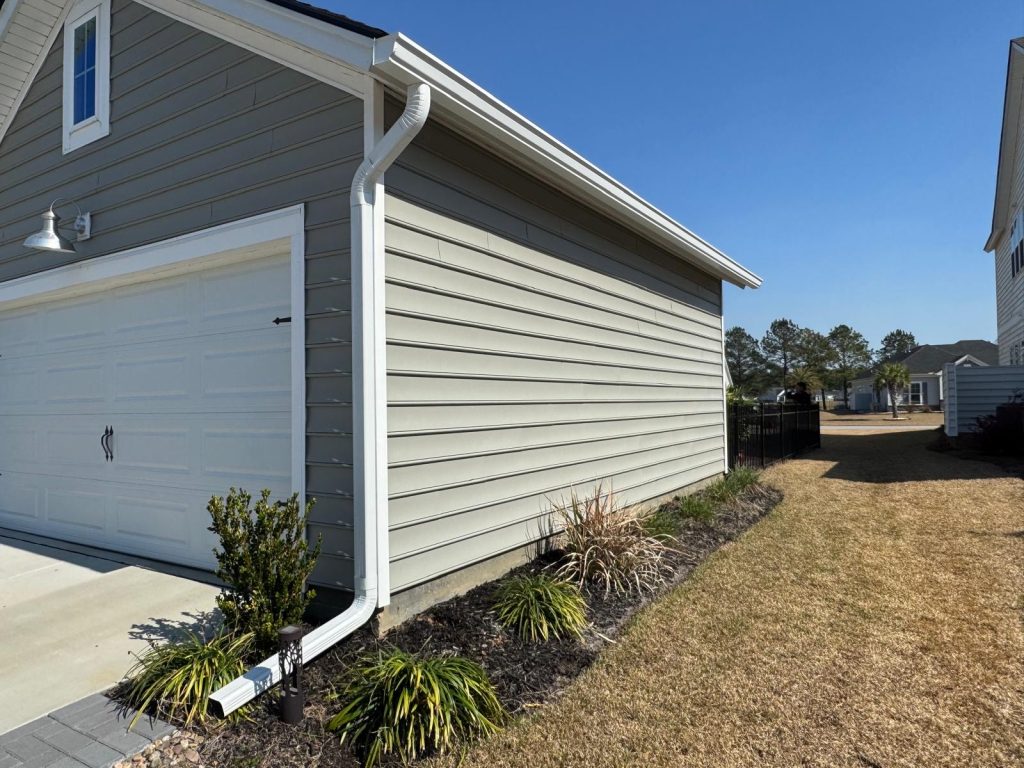 Gray siding home with white trim and gutter system directing water through a downspout near the garage