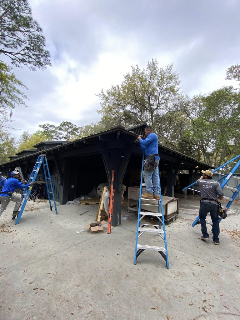 Multiple workers on ladders installing a gutter system along the roofline of a home under construction