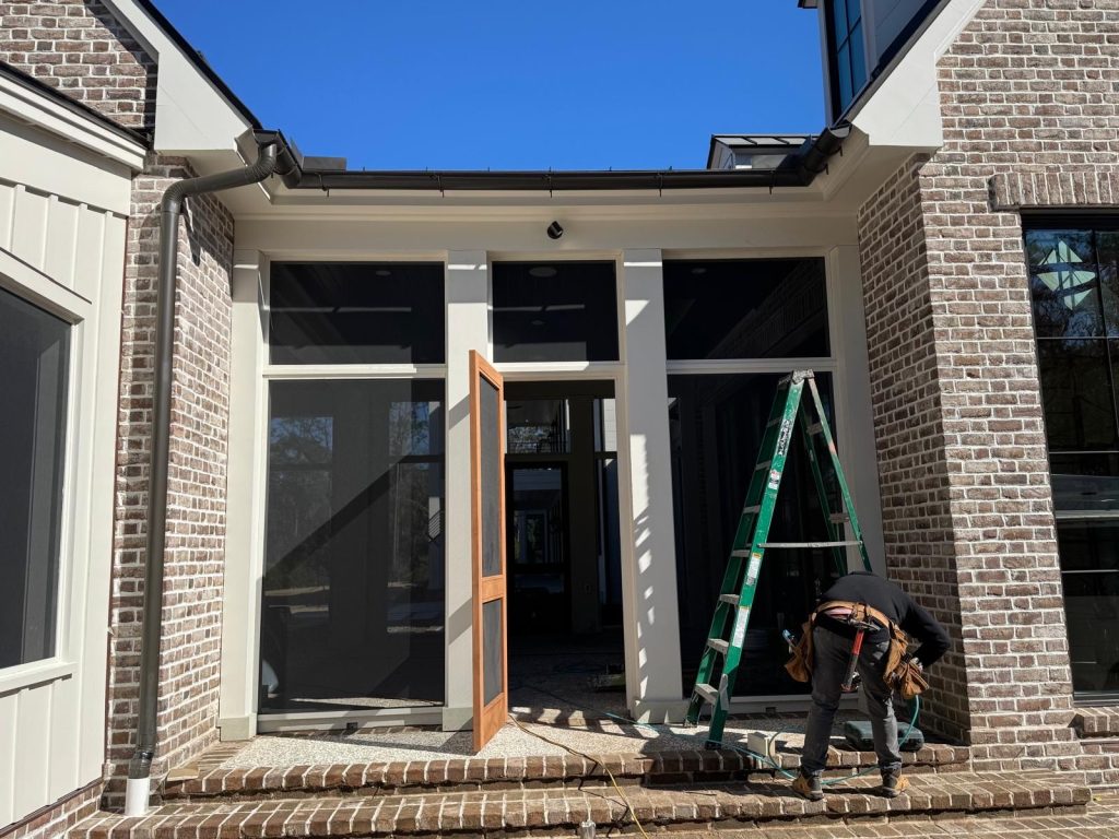 Brick home entry with black gutter system along the roofline and a contractor working near a ladder
